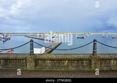 Une digue en béton avec des poteaux d'amarrage en fer et une barrière de chaîne encadrent une vue horizontale du port de Malahide, peuplé de dizaines de voiliers colorés Banque D'Images