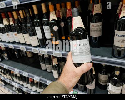 Paris, France - 10 novembre 2023 : POV d'une main masculine tenant une bouteille de vin français de Madiran, millésime 2018, dans un supermarché, mettant en évidence un wi exigeant Banque D'Images