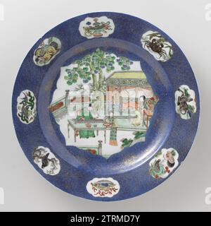 Plat, anonyme, c. 1700 - c. 1720 soucoupe en porcelaine avec mur surélevé et bord incliné, décoré en bleu glacé et sur le glaçage bleu, rouge, vert, jaune, aubergine, noir et or. Le devant du plat est recouvert de bleu pouddré (bleu poudre) avec un grand champ festonné rempli de trois personnes sur une terrasse clôturée avec des rochers et deux arbres, un érudit à une table jouant sur un qin, une femme assise à une table devant un lit, une femme de ménage avec un bol sur un plateau ; le mur avec une décoration dorée sur le bleu avec des pailles de fleurs et des vrilles ; le bord avec une décoration dorée sur l'esprit bleu Banque D'Images