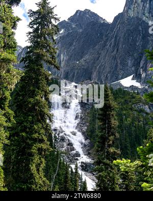 Une chute d'eau en cascade traverse le sentier du lac Wedgemount, encadré par le vert luxuriant des Rocheuses canadiennes. Banque D'Images