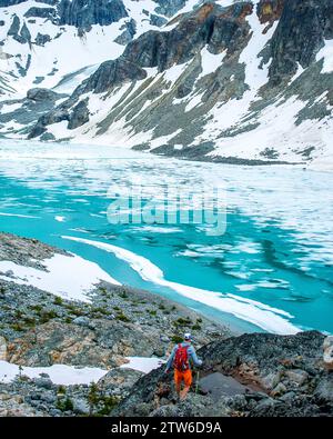 Randonneur solo surplombant les eaux turquoises sereines du lac Wedgemount au milieu des sommets enneigés. Banque D'Images