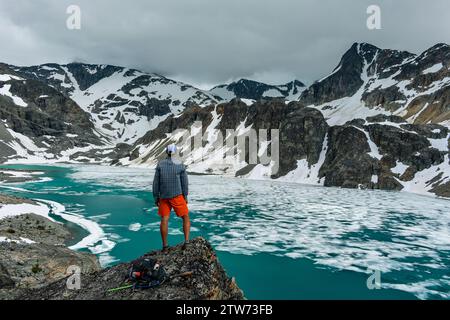 Un randonneur solitaire observe l'étendue glacée du lac Wedgemount, embrassant la solitude. Banque D'Images