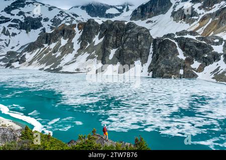 Le randonneur en veste rouge est émerveillé sur le sentier du lac Wedgemount, au milieu d'un magnifique panorama glaciaire. Banque D'Images