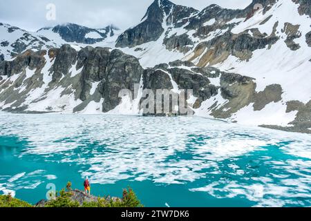 Les randonneurs solitaires regardent l'étendue glacée du lac Wedgemount sous les falaises imposantes. Banque D'Images