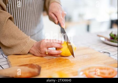 Image rapprochée d'une femme tranchant un citron, préparant des ingrédients et cuisinant dans la cuisine. Cuisine maison, personnes et concepts alimentaires Banque D'Images
