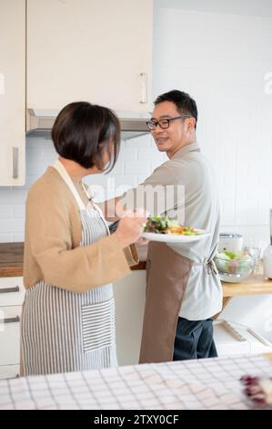 Un charmant couple asiatique aime manger de la nourriture après l'avoir cuisinée ensemble dans la cuisine, passer un bon moment à la maison le week-end. Couples adultes Banque D'Images