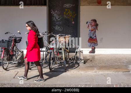 Graffiti d'une fille prenant une photo, une femme marchant devant des vélos garés. Banque D'Images