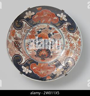 Plat avec un vase à fleurs, huangs feng, shishi et oiseaux, c. 1875 - c. 1925 soucoupe en porcelaine, peinte en bleu glacé et sur le glaçage rouge, noir et or. Sur le plat un double médaillon avec un vase à fleurs avec des chrysanthèmes et des pivoines. Le mur et le bord sont divisés en quatre compartiments avec deux shishi (chien lion) dans un paysage, deux oiseaux sur une branche d'un arbre de prunus et deux fois un cartouche en forme de Ruyi avec un Fenghuang sur un fond bleu avec des vignes fleuries. Le plat est pris dans un cadre métallique. Probablement un européen (français ?) Imitation de l'Imari japonais. Europe porcelaine. Glaçage. C Banque D'Images