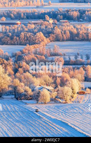 Voiture conduisant sur une route enneigée dans une vue de paysage hivernal Banque D'Images