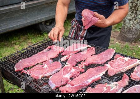 mains d'un cuisinier plaçant des morceaux de bœuf crus sur un gril Banque D'Images