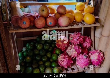 Une délicieuse gamme de fruits du dragon vibrants, de limettes vertes et de bananes mûres habilement exposées sur une étagère en bois dans une boutique écologique. Banque D'Images