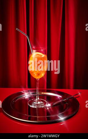 grand verre rempli de cocktail orange, aperol avec des glaçons décoré morceau d'agrumes et de paille assis sur un plateau d'argent Concept de fête. Banque D'Images