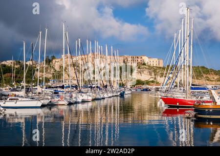 Bateaux à voile à l'ancre dans le port et le port de plaisance de Tropea, les maisons de la ville sur une falaise rocheuse au loin. Banque D'Images