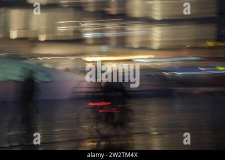 Longue exposition de pédastriens méconnaissables et cyclistes dans la rue la nuit dans un cadre urbain Banque D'Images