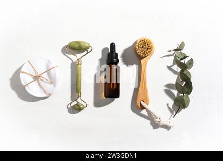 Rouleau de massage du visage, sérum, tampons de coton et brosse sur fond blanc clair. Beauté divers produits cosmétiques et de soins de la peau respectueux de l'environnement. Vue de dessus. Co Banque D'Images