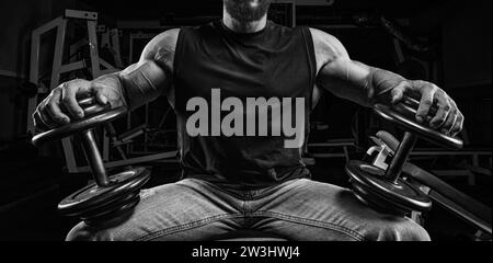 Homme musclé assis sur un banc avec des haltères dans la salle de gym. Concept de fitness et de musculation. Supports mixtes Banque D'Images