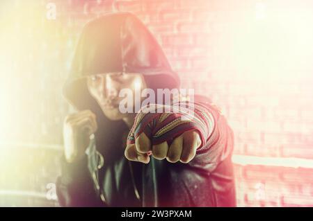 Boxeur dans un sweat-shirt noir et bandages blessé sur ses mains bat son poing en avant. Le concept de sports, gymnases, clubs de boxe. Supports mixtes Banque D'Images