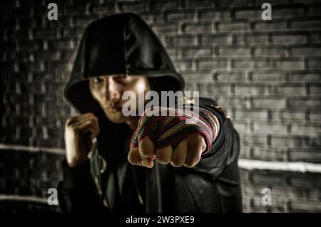 Boxeur dans un sweat-shirt noir et bandages blessé sur ses mains bat son poing en avant. Le concept de sports, gymnases, clubs de boxe. Supports mixtes Banque D'Images