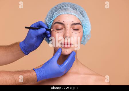 Médecin dessinant des marques sur le visage de la femme pour l'opération de chirurgie esthétique sur fond beige Banque D'Images