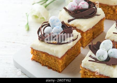 Barres de gâteau aux carottes de Pâques décorées avec nid de chocolat et œufs de bonbons au chocolat fleurissant des fleurs de cerise ou de pomme sur des fonds rustiques en bois clair. Banque D'Images