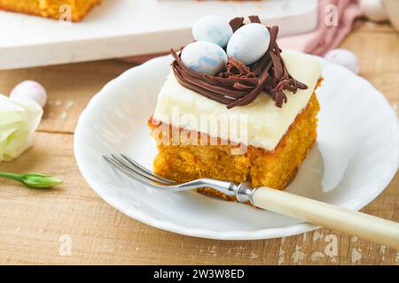 Barres de gâteau aux carottes de Pâques décorées avec nid de chocolat et œufs de bonbons au chocolat fleurissant des fleurs de cerise ou de pomme sur des fonds rustiques en bois clair. Banque D'Images