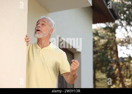 Homme âgé en colère montrant le poing près de la maison, espace pour le texte. Voisin ennuyeux Banque D'Images