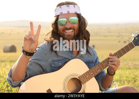 Heureux homme hippie avec guitare montrant signe de paix dans le champ Banque D'Images