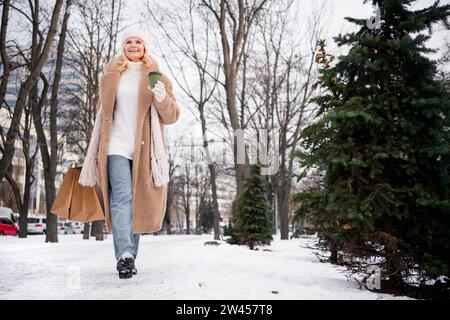 Photo de femme attrayante excitée porter manteau beige appréciant vin chaud acheter des cadeaux à l'extérieur du parc urbain de la ville Banque D'Images