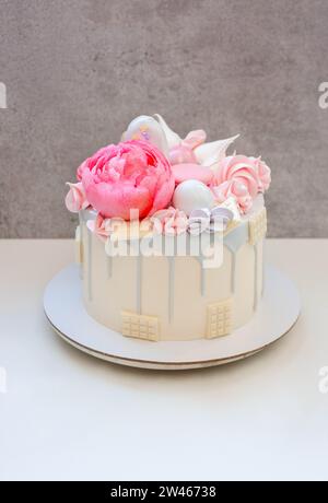 Beau et élégant gâteau décoré de chocolat gris fondu, macarons, fleur de pivoine rose comestible, bouchées de chocolat et meringues Banque D'Images