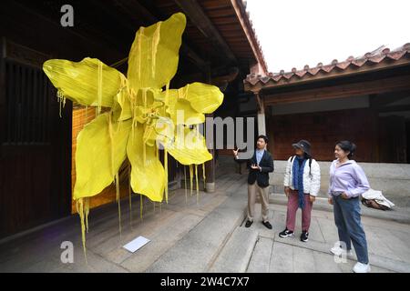 JINJIANG, 21 décembre 2023 (Xinhua) -- Wu Shaopeng (L), conservateur d'art et descendant de Chinois d'outre-mer, présente son installation artistique aux touristes dans un bâtiment historique du village de Wulin de Jinjiang, dans la province du Fujian, dans le sud-est de la Chine, le 19 décembre 2023. Dans le village de Wulin, dans la province du Fujian de l'est de la Chine, les visiteurs sont souvent fascinés par le mélange de styles architecturaux : maisons locales en briques rouges, bâtiments gothiques, structures gréco-romanes et bâtiments mêlant éléments chinois et occidentaux. Le mélange éclectique de styles architecturaux raconte de façon vivante l'histoire de la vill Banque D'Images