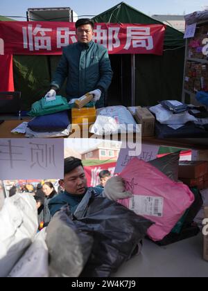 (231221) -- JISHISHAN, 21 décembre 2023 (Xinhua) -- cette photo combinée montre Zhao Yushan, facteur de China Post, dans une colonie temporaire (en haut) et Zhao Yushan trie les colis dans la colonie temporaire du village de Dahe, dans le comté de Jishan, dans la province du Gansu, au nord-ouest de la Chine, le 21 décembre 2023. Les opérations de secours en bon ordre se poursuivent dans la province de Gansu, frappée par le séisme. (Xinhua/Chen Bin) Banque D'Images