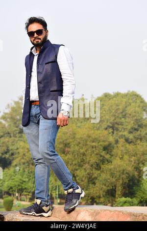 Homme modèle indien élégant dans des vêtements décontractés chemise blanche noire avec veste bleue et lunettes de soleil photo parfaite pour un usage commercial. Banque D'Images