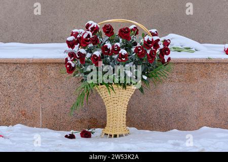 Panier avec des roses rouges couvertes de stands de neige au mémorial en hiver Banque D'Images