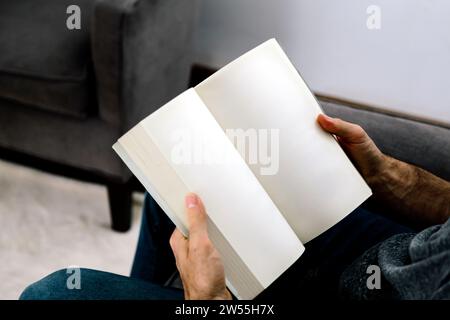 Homme lisant un livre. Photo idéale du livre de pages vierges prêt pour la maquette. Homme assis dans un salon tenant un livre ouvert dans ses mains. Banque D'Images