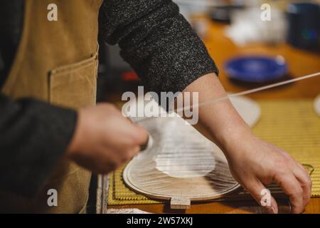 Luthier fabricant de luth méconnaissable artisan à deux mains exécutant le processus de bandes de ronflage de contrôleur de courbure dans l'outil de fer pour un nouveau dos et avant brut Banque D'Images