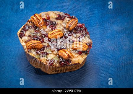 gâteau au rhum de vacances avec pacanes, ananas, cerises séchées et canneberges sur papier bleu art. Banque D'Images