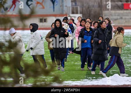 BEITUN, 21 déc. 2023 (Xinhua) -- des étudiants courent pour se réchauffer dans un collège de la ville de Beitun, dans la région autonome ouïgour du Xinjiang, au nord-ouest de la Chine, 20 déc. 2023. Situé au pied sud des montagnes Altay, Beitun City possède d'abondantes ressources de glace et de neige, favorisant la croissance rapide dans les sports de glace et de neige, les industries, et le tourisme. ces dernières années, les écoles primaires et secondaires locales ont pleinement exploité ces ressources et avantages géographiques en intégrant les sports de glace et de neige dans leurs programmes d’enseignement. (Xinhua/Ding Lei) Banque D'Images