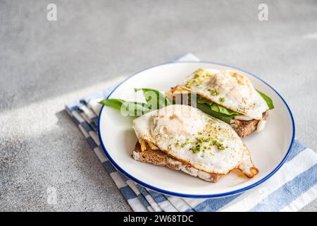 Angle élevé de l'assiette de pain grillé appétissant avec des feuilles d'épinards frais oeufs frits sauce pesto servi sur serviette bleue Banque D'Images