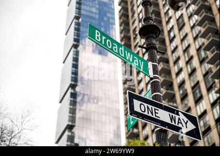 Angle faible de la direction de l'emplacement de Broadway et panneaux de signalisation à sens unique fixés sur le poteau de signalisation contre les immeubles de grande hauteur floutés avec des murs de verre à Manhatta Banque D'Images