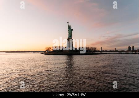 Vue pittoresque de la statue de la liberté situé sur la côte de la rivière tranquille contre le ciel nuageux de coucher de soleil à New York Banque D'Images