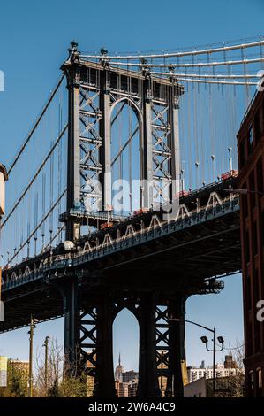 Une scène de rue animée à DUMBO, Brooklyn, capturant l'emblématique Manhattan Bridge encadré entre deux bâtiments historiques en briques. Banque D'Images