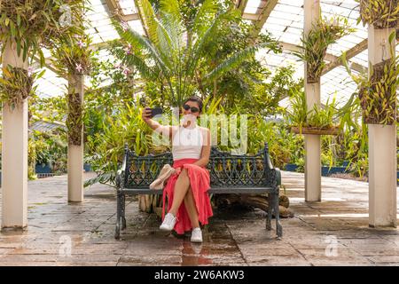 Une femme se détend tout en prenant un selfie avec smartphone et en profitant de la beauté du jardin botanique de la forêt Chapultepec et de la serre, entouré par Banque D'Images