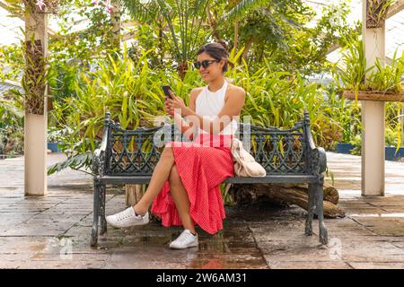 Une femme profite d'un moment de calme sur un banc avec son smartphone entouré d'une verdure luxuriante dans le jardin botanique de la forêt Chapultepec et serre, moi Banque D'Images