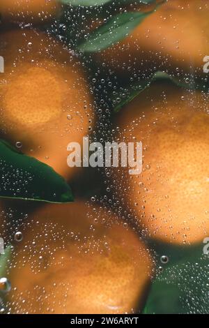 Vue rapprochée d'oranges vibrantes avec des feuilles, agrandies et déformées à travers des gouttelettes d'eau claires, créant une image abstraite et rafraîchissante. Banque D'Images