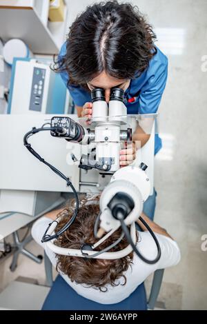 Vue de dessus d'un médecin féminin anonyme en uniforme médical et avec stéthoscope regardant loin tout en étant assis avec un patient masculin anonyme au biomi de lampe fendue Banque D'Images