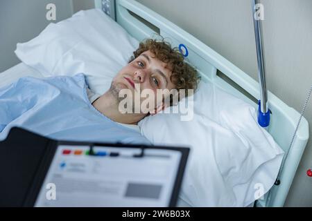 Vue de dessus d'une femme médecin anonyme avec presse-papiers debout près du patient couché sur le lit regardant la caméra à l'hôpital Banque D'Images