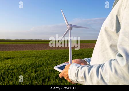 Vue latérale de la section médiane de l'homme tenant le modèle d'éolienne sur le champ agricole contre le ciel bleu Banque D'Images