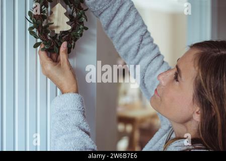 Gros plan d'une femme accrochant une couronne de Noël au mur Banque D'Images