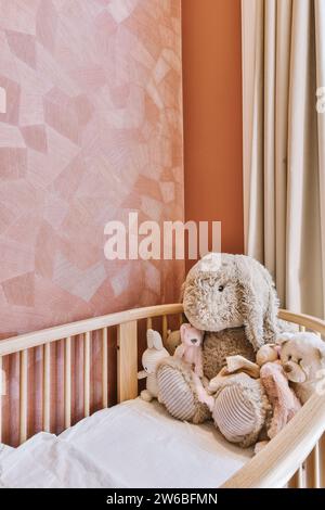 Berceau confortable avec divers jouets en peluche par papier peint rose dans la pépinière à la maison contemporaine Banque D'Images