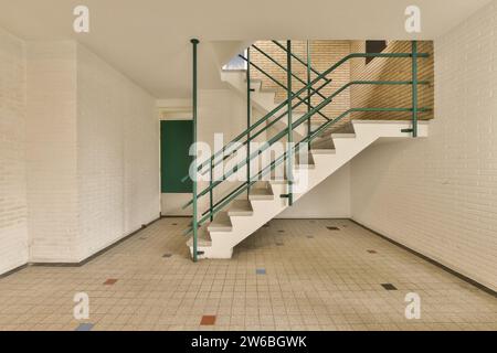 Immeuble de bureaux avec escalier vide et main courante verte menant au deuxième étage entouré de murs blancs et sol carrelé Banque D'Images